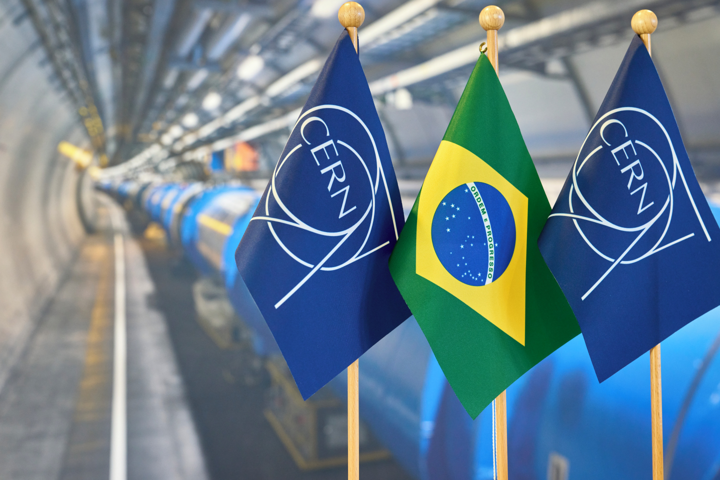As Brazil becomes Associate Member State of CERN, the Brazilian flag is photographed along with the CERN flag. In the back, we can see the Large Hadron Collider, CERN's flagship accelerator.